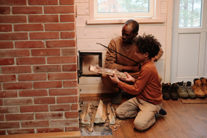 Son helping father put wood recommended by Barnegat chimney service pro into a wood burning stove