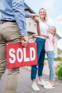 SOLD sign in the hand of a Seaside Park real estate agent handing keys over to new owner.