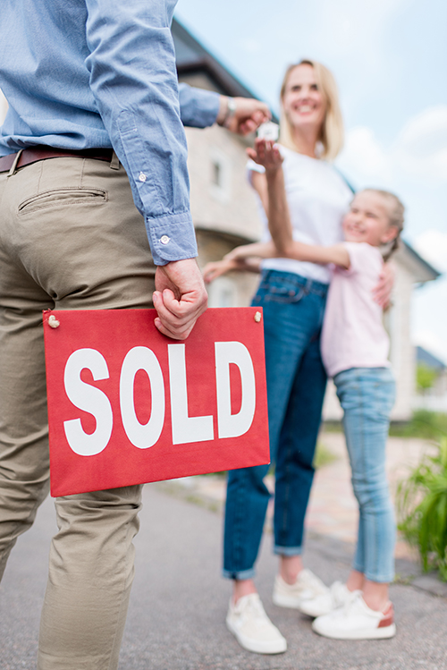 SOLD sign in the hand of a Seaside Park real estate agent handing keys over to new owner.