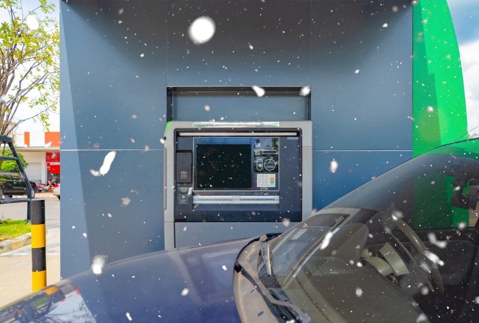 Drive-up ATM in falling snow as a car pulls up, an example of self-service banking that depends on dependable ATM maintenance
