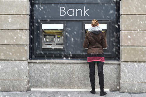 Woman using an outdoor bank ATM in the snow, showing why reliable ATM service in New Jersey matters year-round